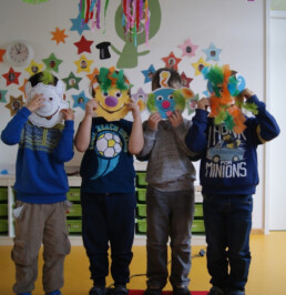 Vier Kinder halten sich selbst gebastelte Masken vor das Gesicht