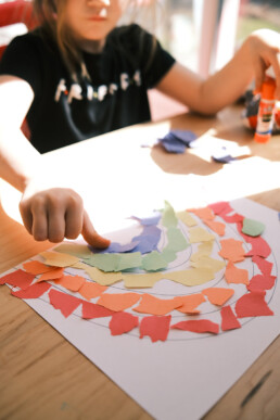 Mädchen bastelt ein Regenbogen-Bild mit Papierschnipseln