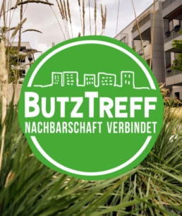 Das Logo des Nachbarschaftstreffs am Butzweilerhof vor dem Hintergrund der Häuser in Ossendorf
