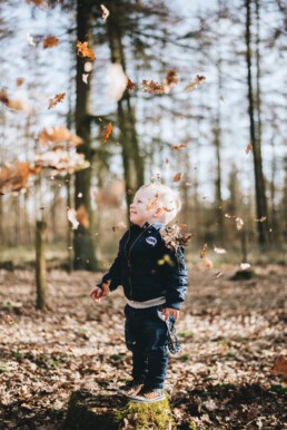 Kleinkind im herbstlichen Laubwald, trockene Blätter wirbeln umher