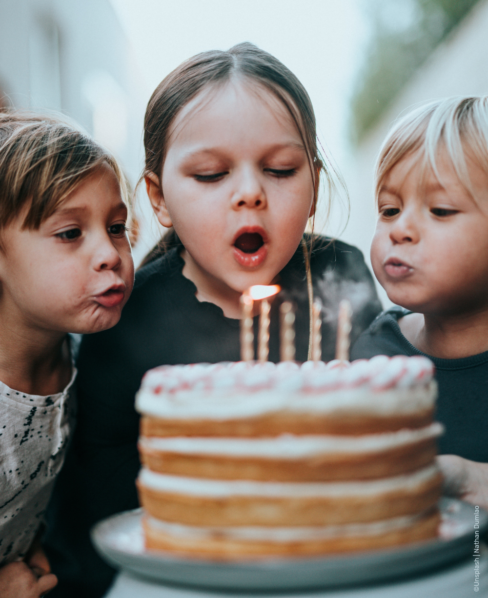 Drei Kinder pusten gemeinsam die Kerzen einer Geburtstagstorte aus