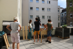Die Terrasse im Sonnenschein, das Filmteam filmt den Aufbau eines Hochbeetes aus Holz